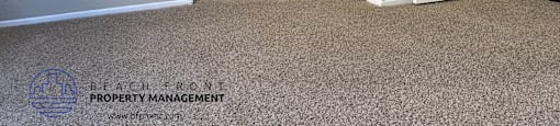 A carpeted room with a door and a mirror.
